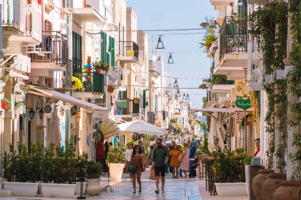 Street in Polignano a Mare with some people walking and some plants on the sides